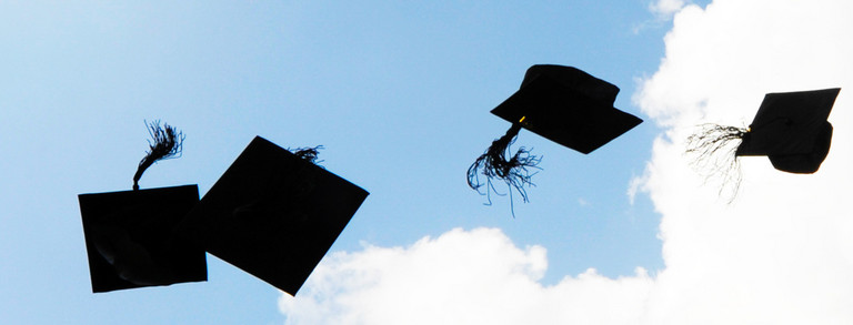 Vier schwarze Doktorhüte fliegen in die Luft vor blauem Himmel mit weißen Wolken.